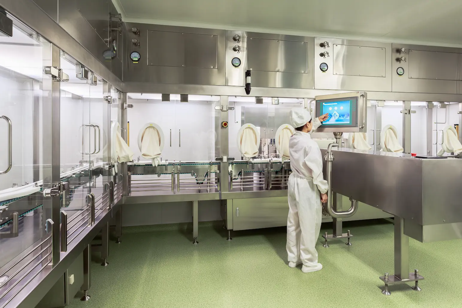 Technician in cleanroom suit operating touchscreen control panel inside JYMed Peptide’s Shenzhen FDF facility sterile isolator line.